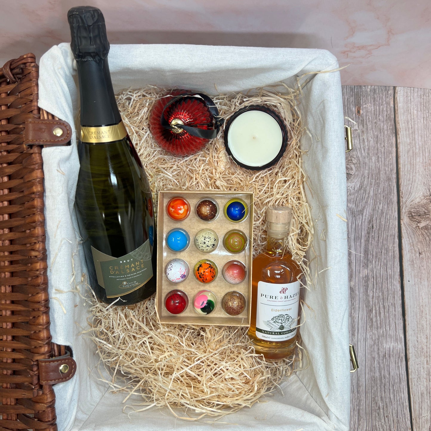 Gift basket with wine bottles, candles, and decorative items on a wooden surface.