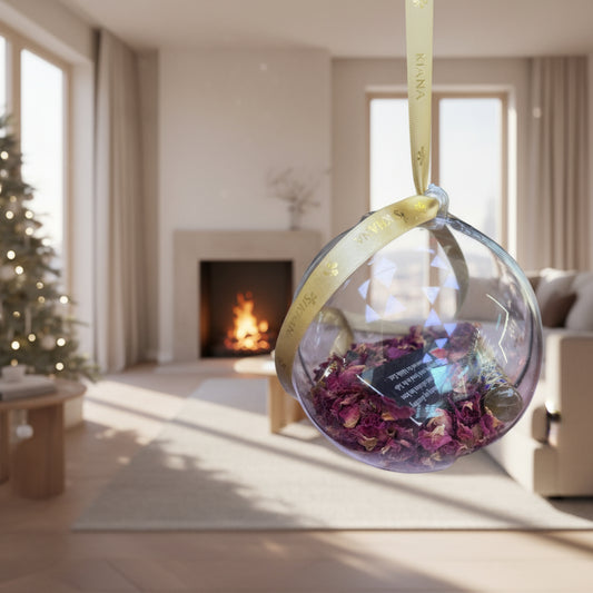 Decorative glass sphere with dried flowers and a gold ribbon on a textured surface and 4 x 3ml body sprays