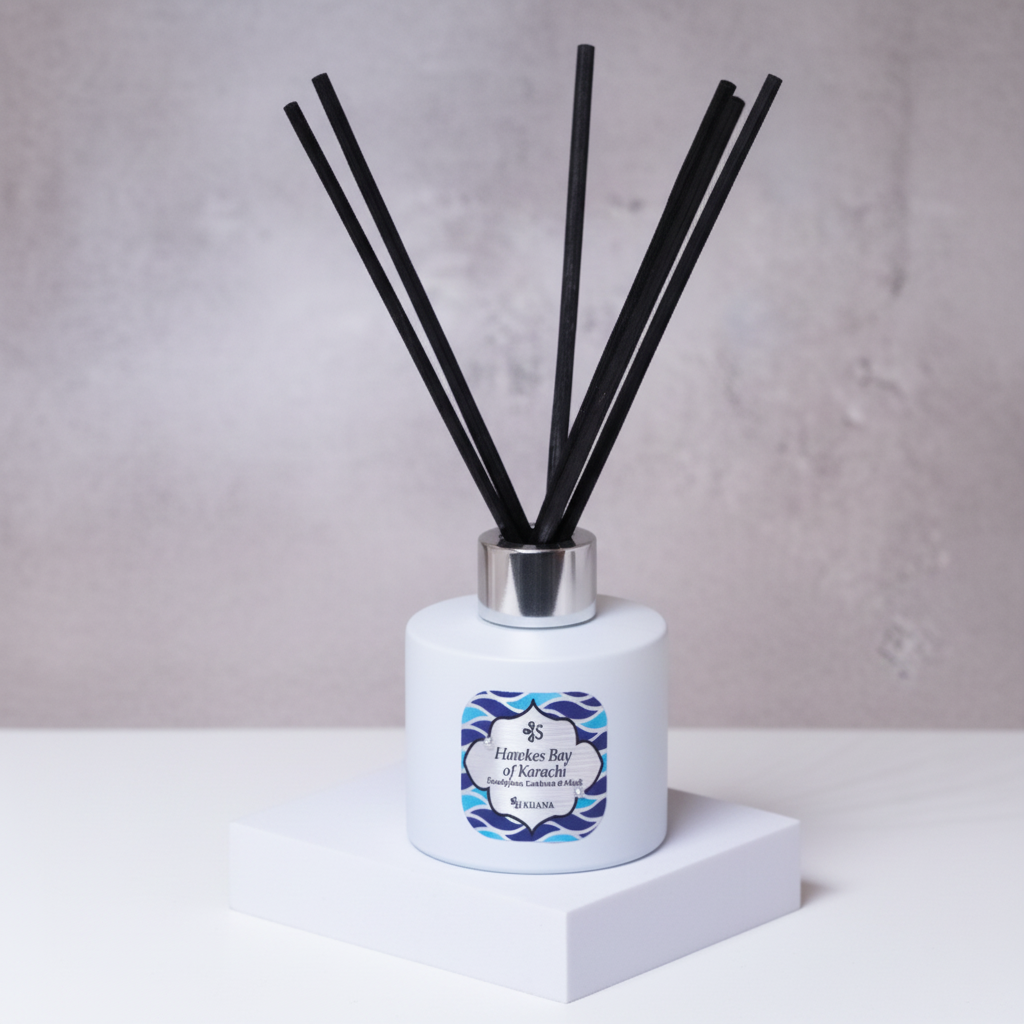 Diffuser with reeds and a decorative label on a white surface with green leaves in the background