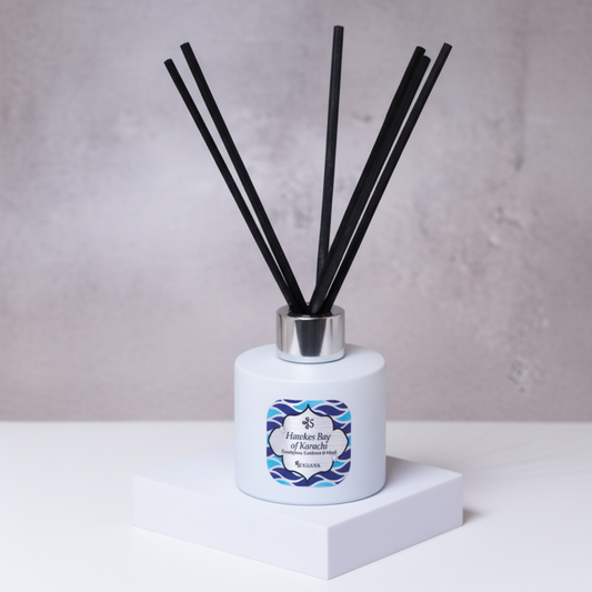 Diffuser with reeds and a decorative label on a white surface with green leaves in the background