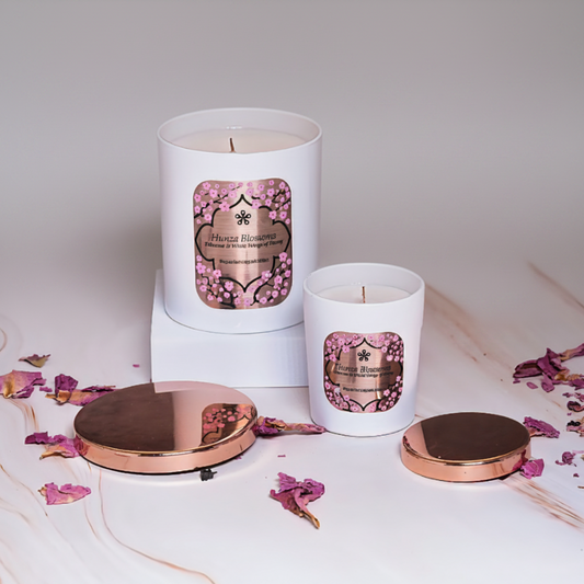 Two white candles with pink labels on a marble surface with rose petals.