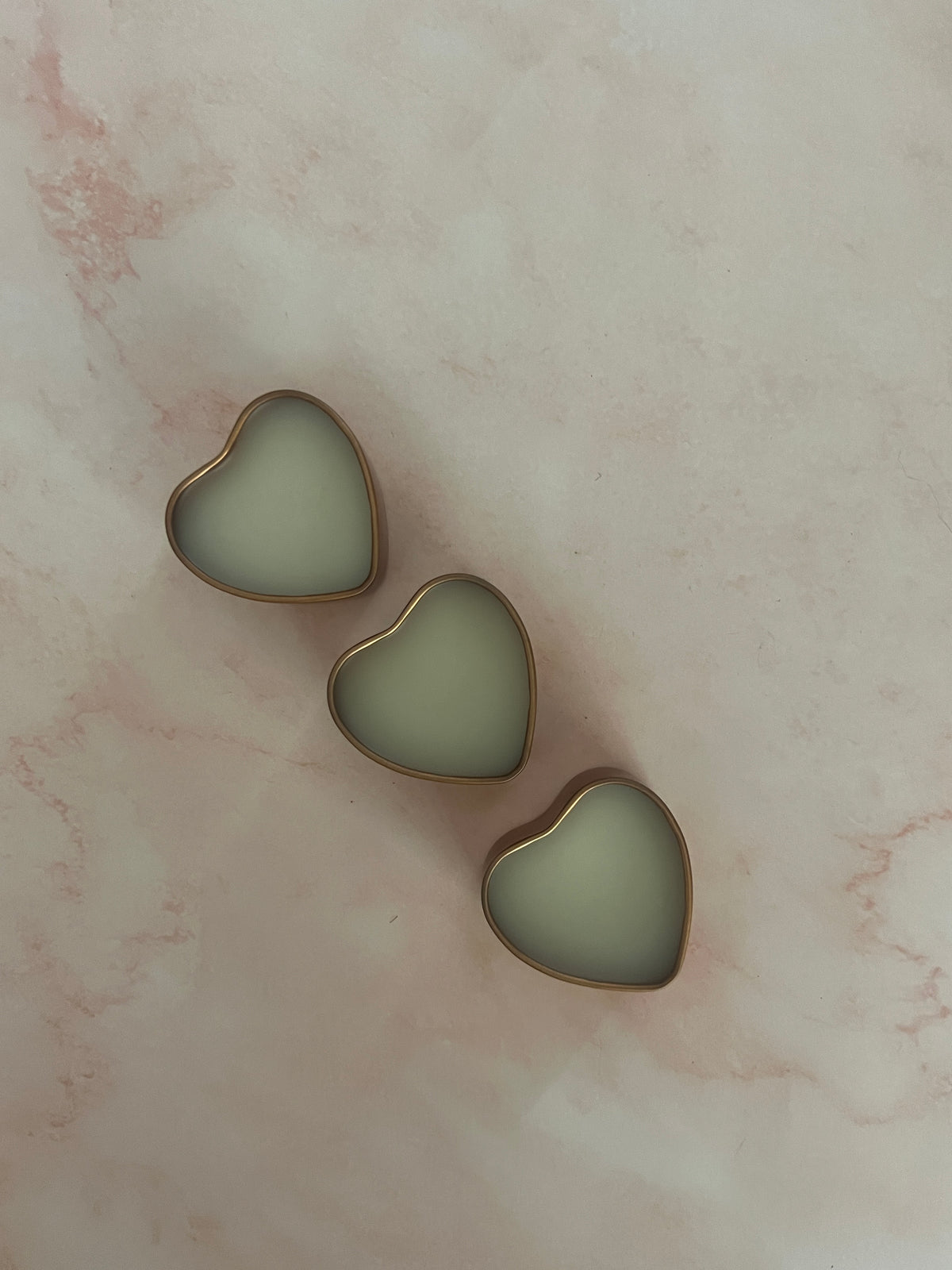Three gold heart-shaped jars of solid perfume with lids removed