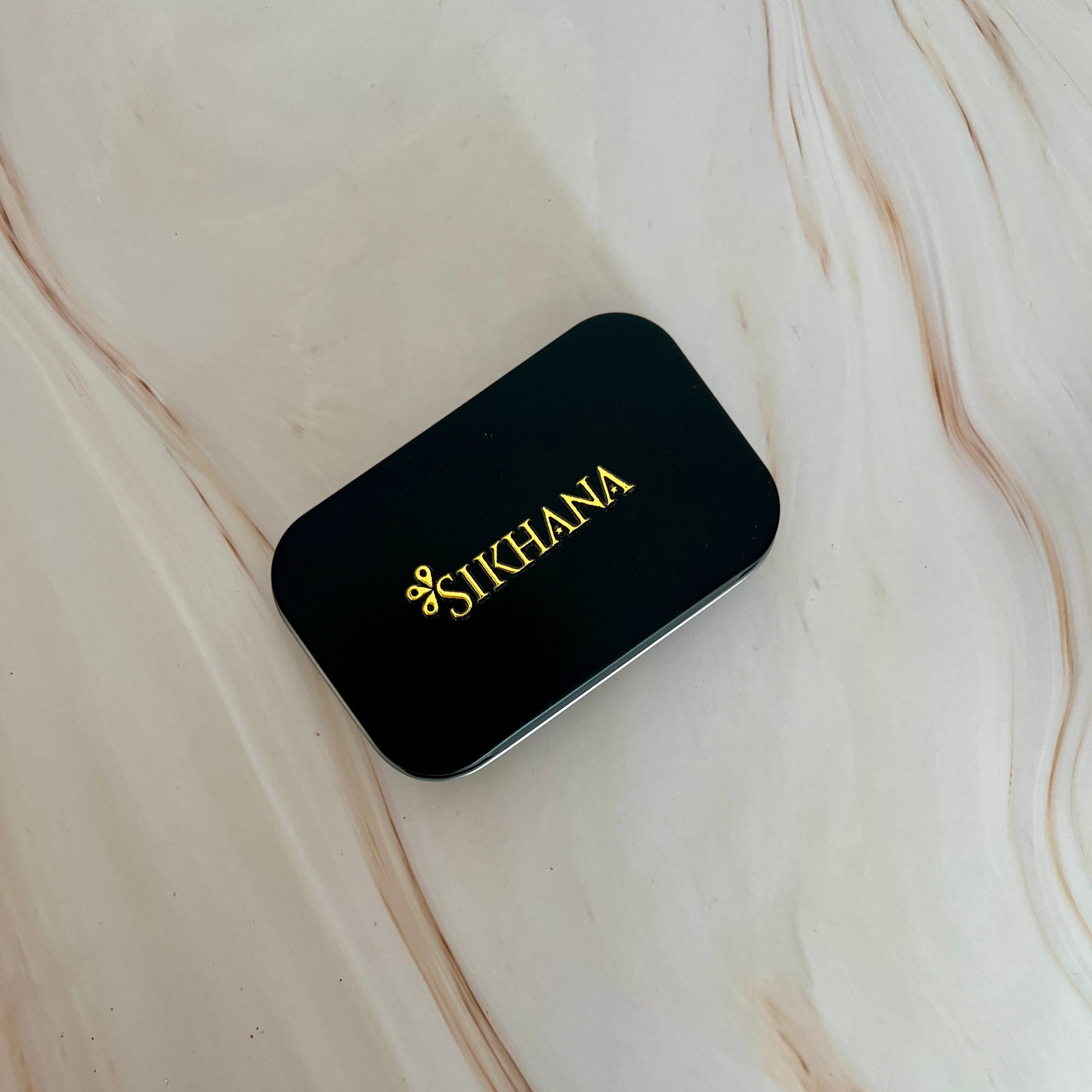 Black scent case with 'Sikhana' branding on a marble surface