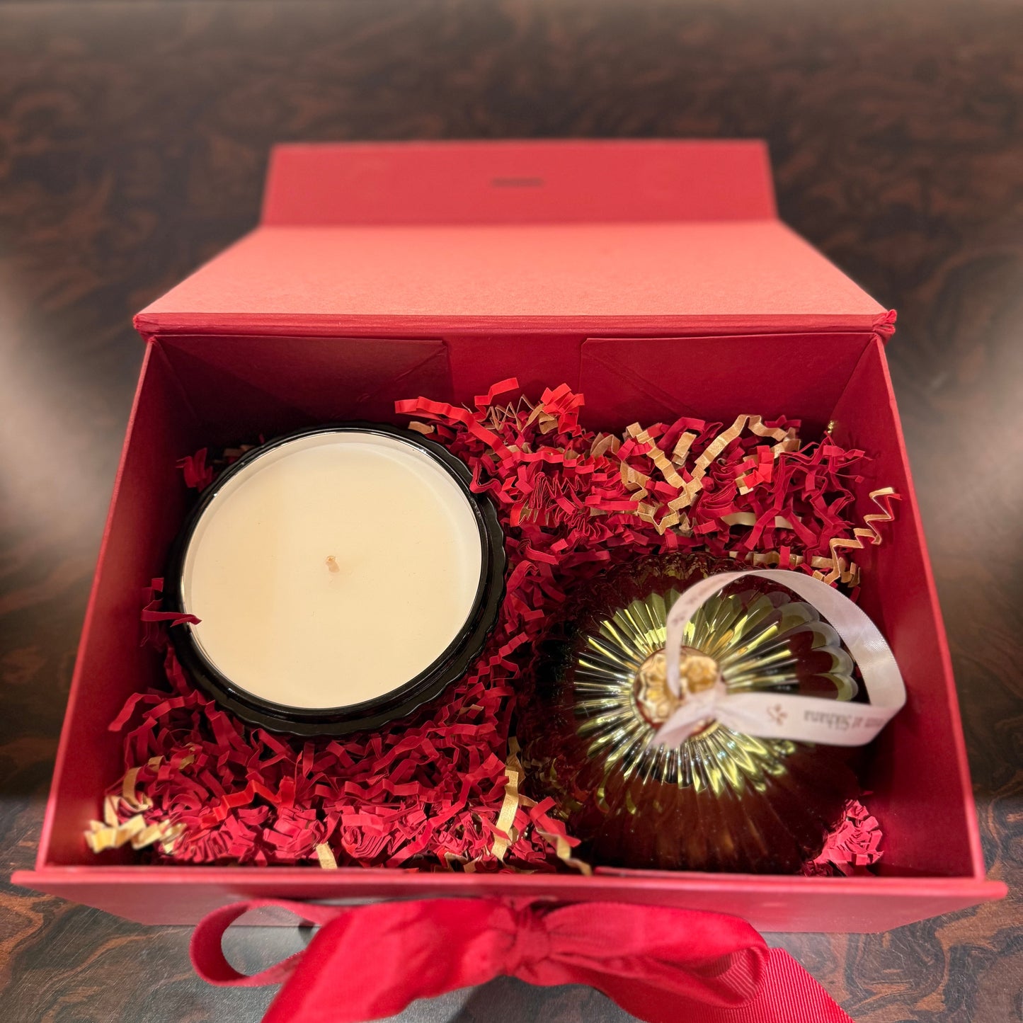Gift set with a candle and decorative ball in a red box on a textured surface.