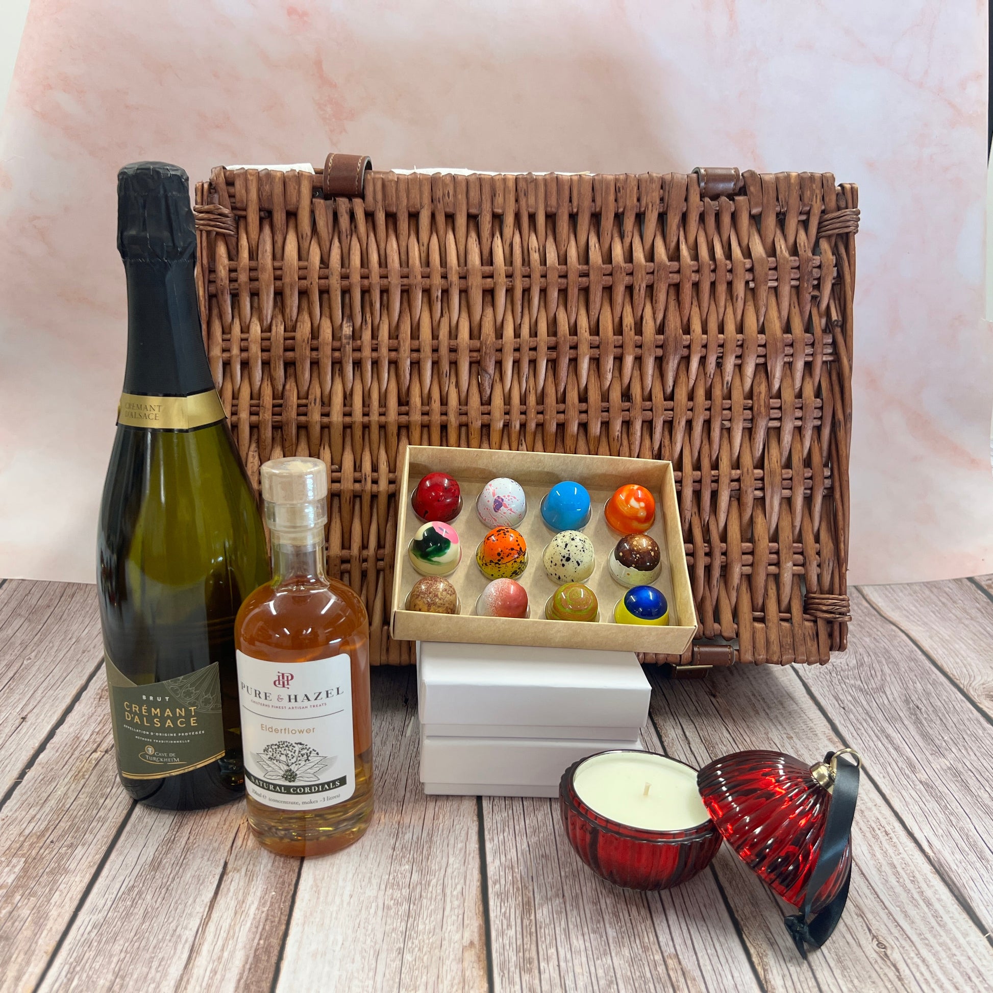 Wicker picnic basket with bottles, a candle, and decorative items on a wooden surface.