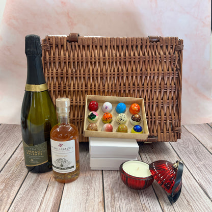 Wicker picnic basket with bottles, a candle, and decorative items on a wooden surface.