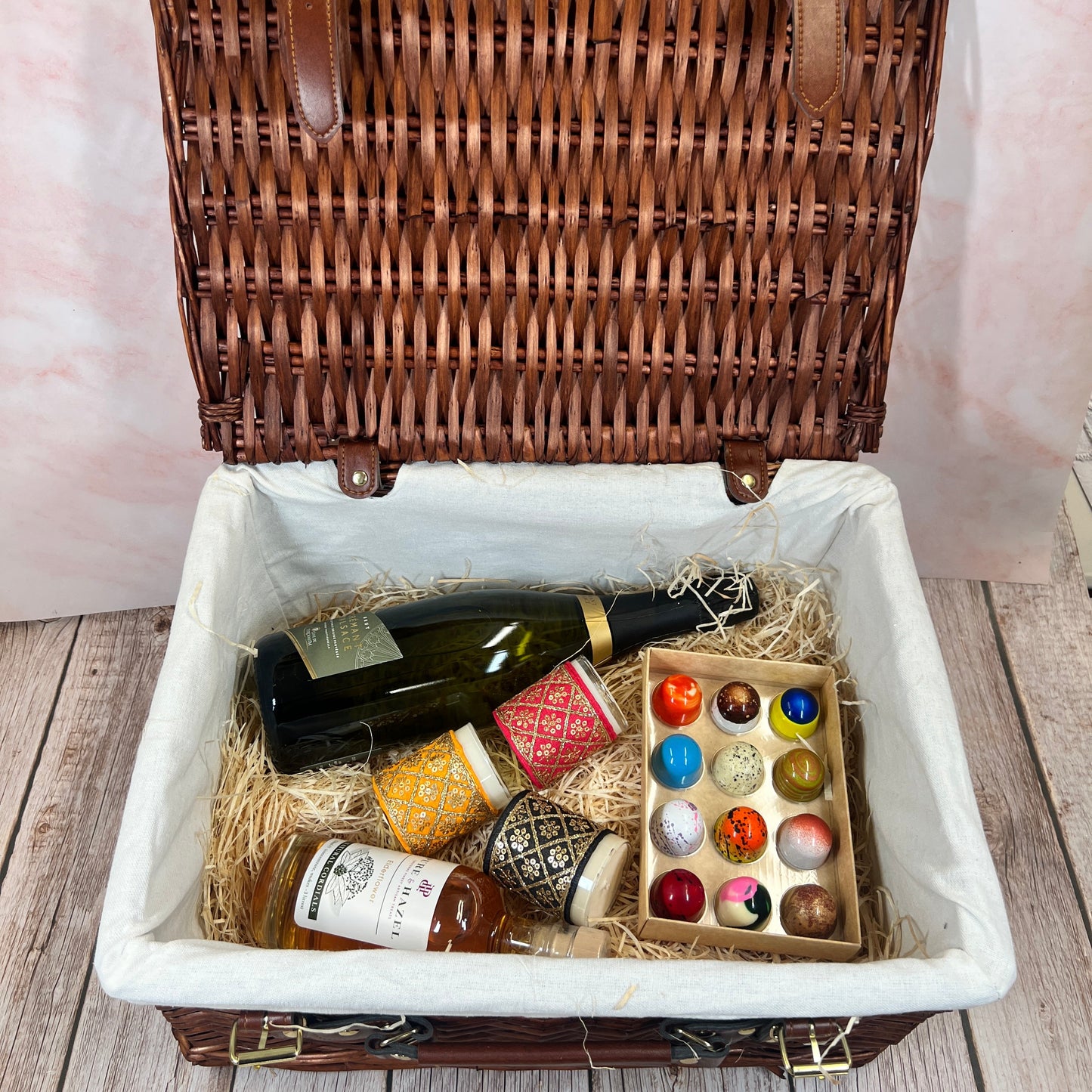 Open wicker picnic basket with wine, cheese, and crackers on a wooden surface.