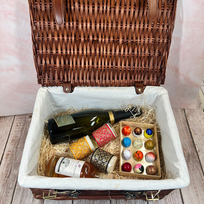 Open wicker picnic basket with wine, cheese, and crackers on a wooden surface.