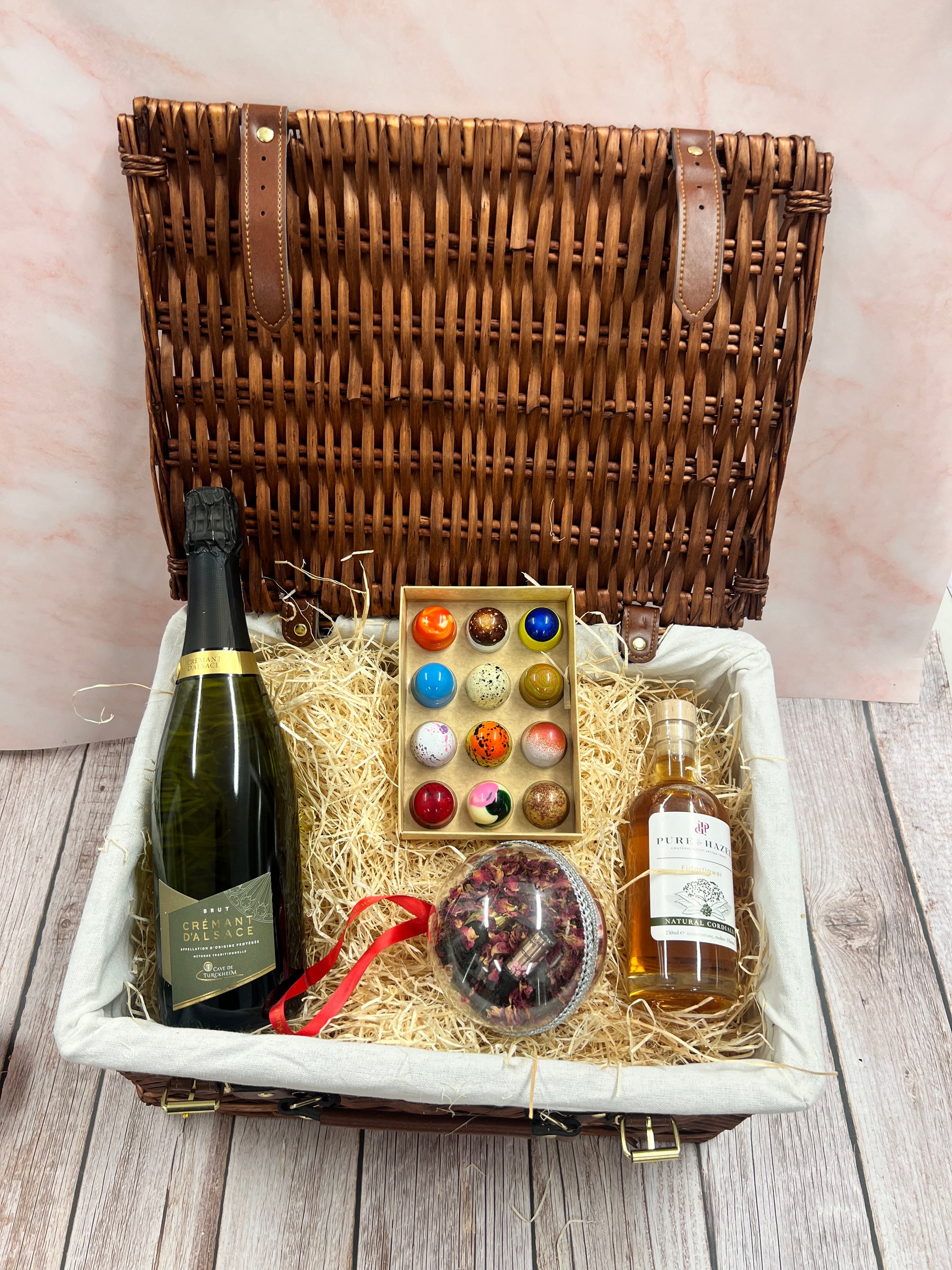 Gift basket with wine, chocolates, and a decorative item on a wooden surface.