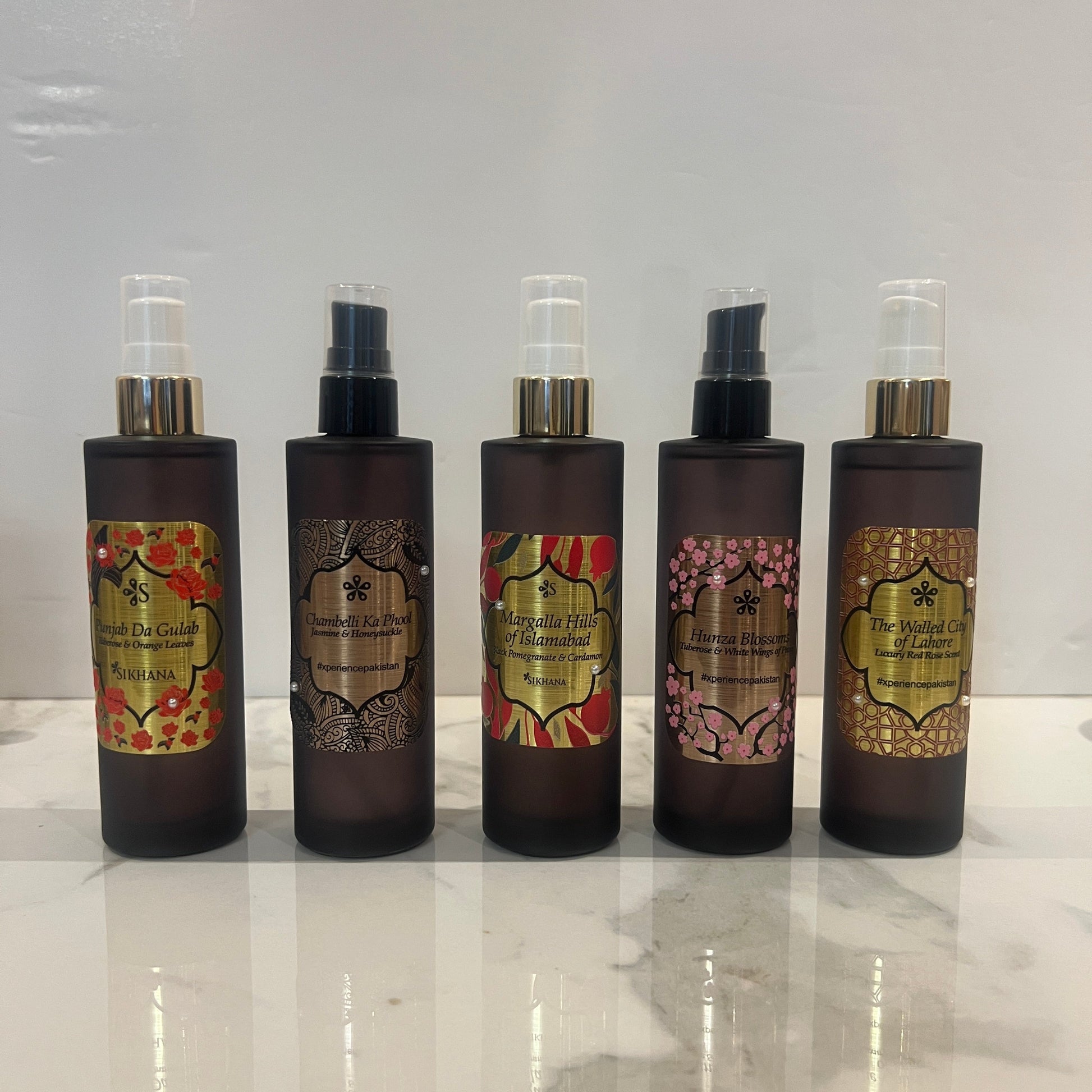 Set of five black bottles with decorative labels on a reflective surface. Flora