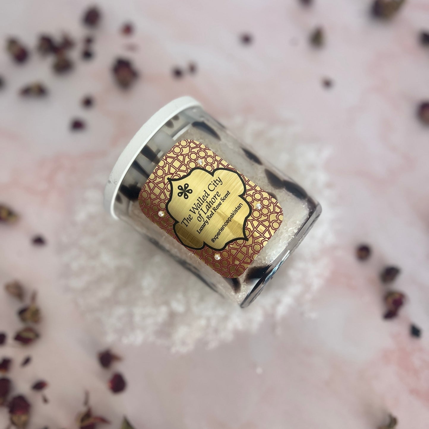 Small jar with a decorative label on a textured surface with dried herbs.