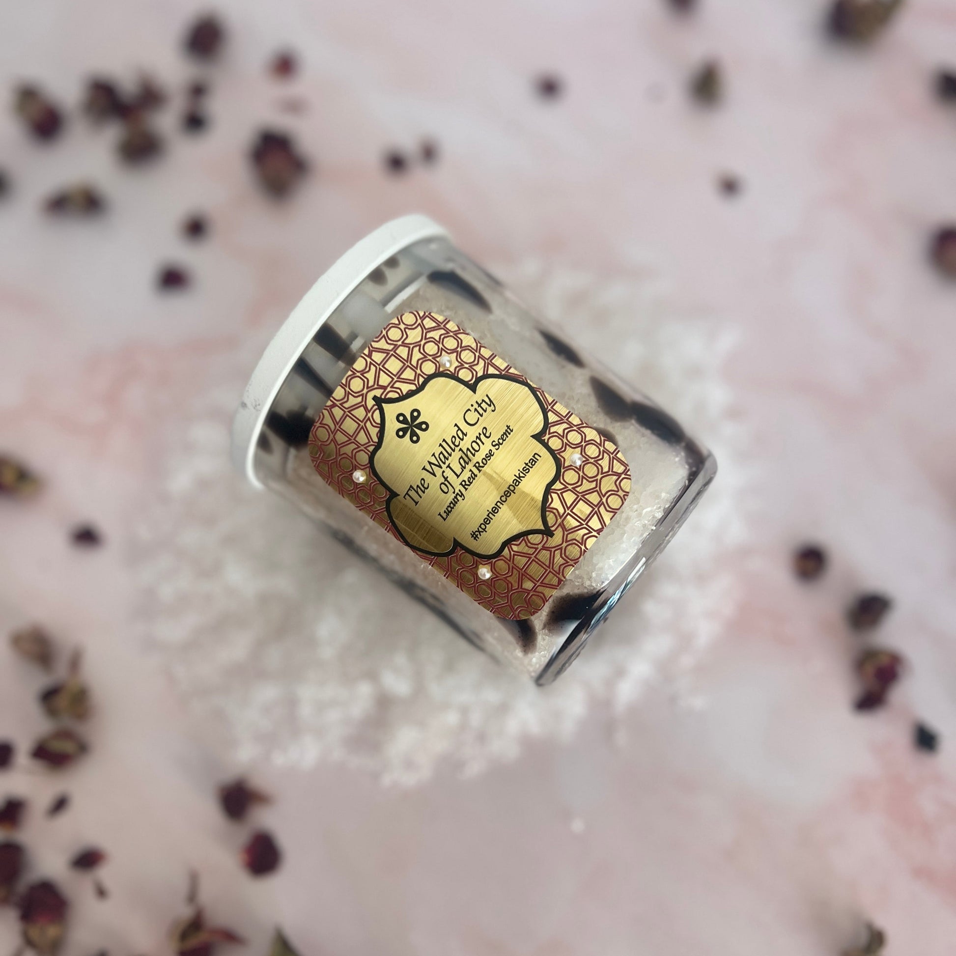 Small jar with a decorative label on a textured surface with dried herbs.