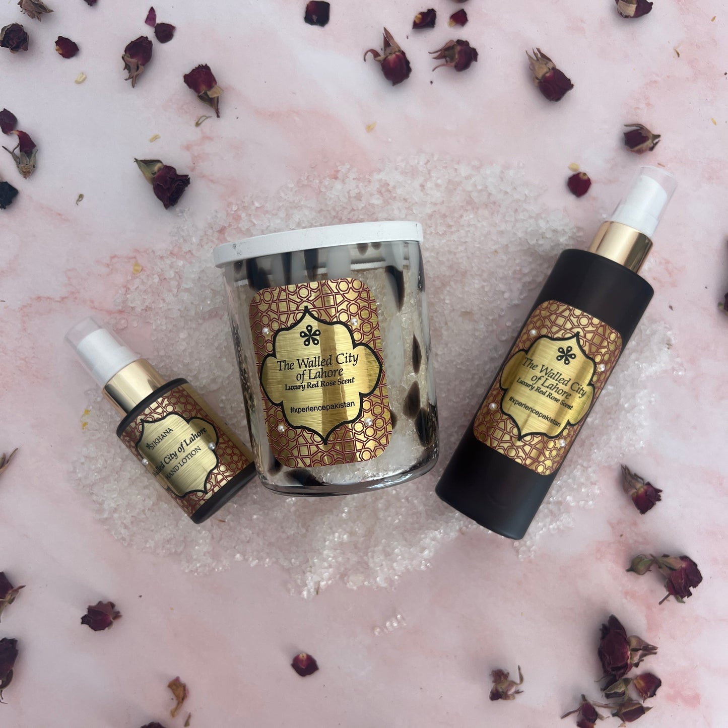 Three skincare bottles with gold labels on a pink textured background with dried flowers.