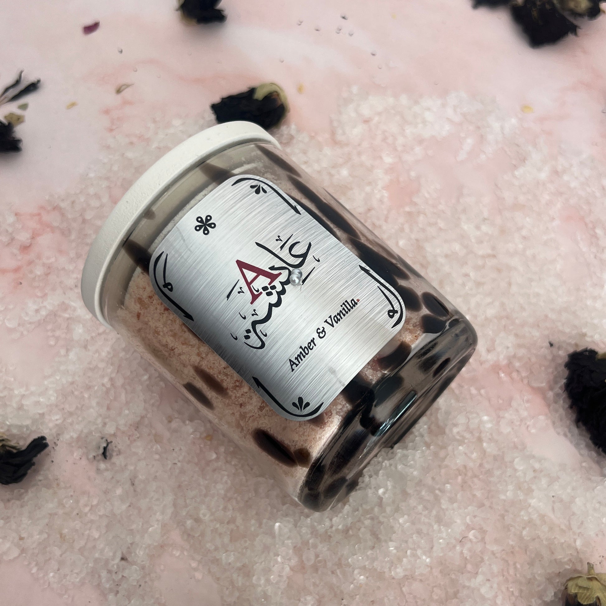 Bath Salts in a glass jar with a label on a textured pink surface with black decorative elements.