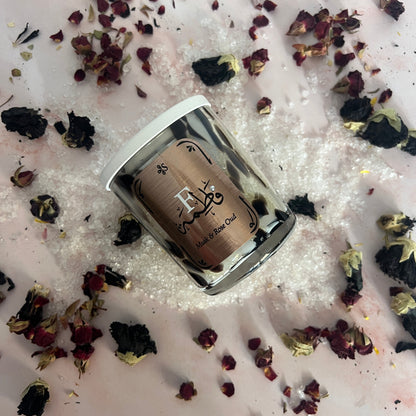 Small container with a decorative label on a bed of pink bath salts and dried flowers.