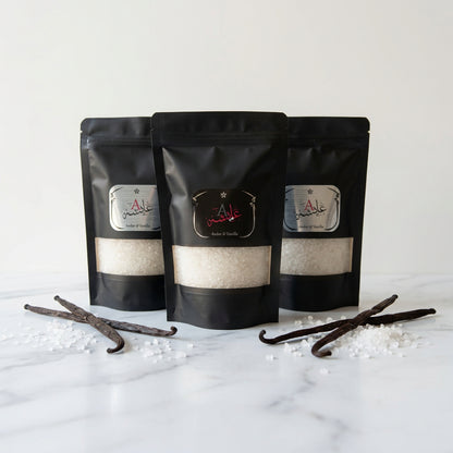 Three black stand-up pouches of a product with silver and red labels, displayed on a glass-topped side table in a bedroom setting.