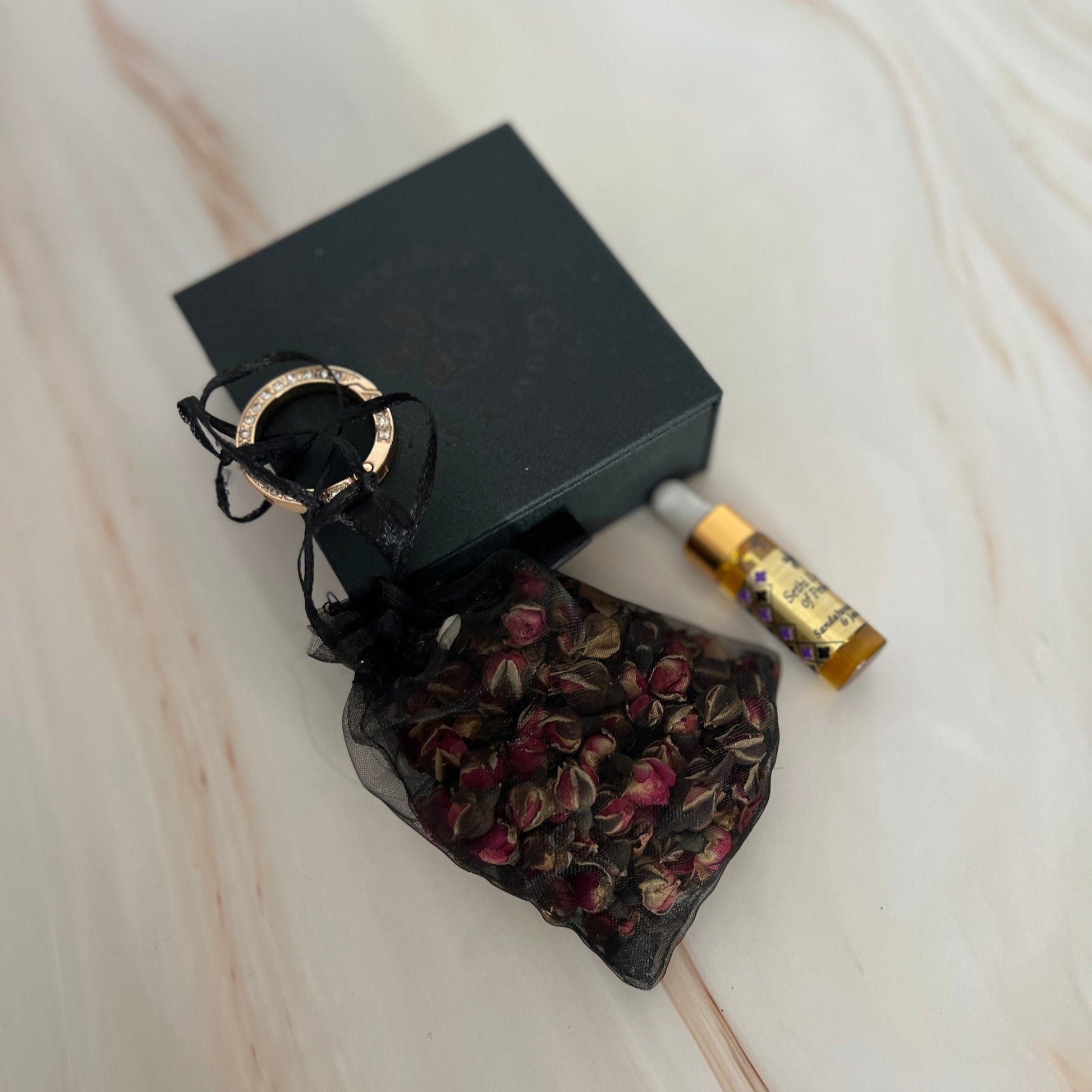 Black decorative bag with dried flowers, black box, and small 5ml dropper bottle on a light wooden surface